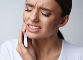 oung female showing tooth pain by placing hand on her mouth's right side at Pike District Smiles.