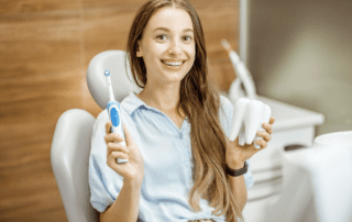 patient sitting on dental chair and holding toothbrush and tooth model
