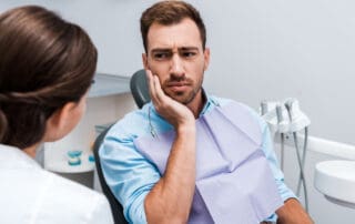 Patient in pain sitting in front of the dentist, placing hand on mouth indicating the side of pain.