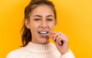 Teenage girl placing Invisalign aligners on her teeth.