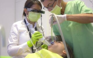 Two focused dentists administering treatment to a patient lying on a bed, placing dental instruments in the patient's mouth.