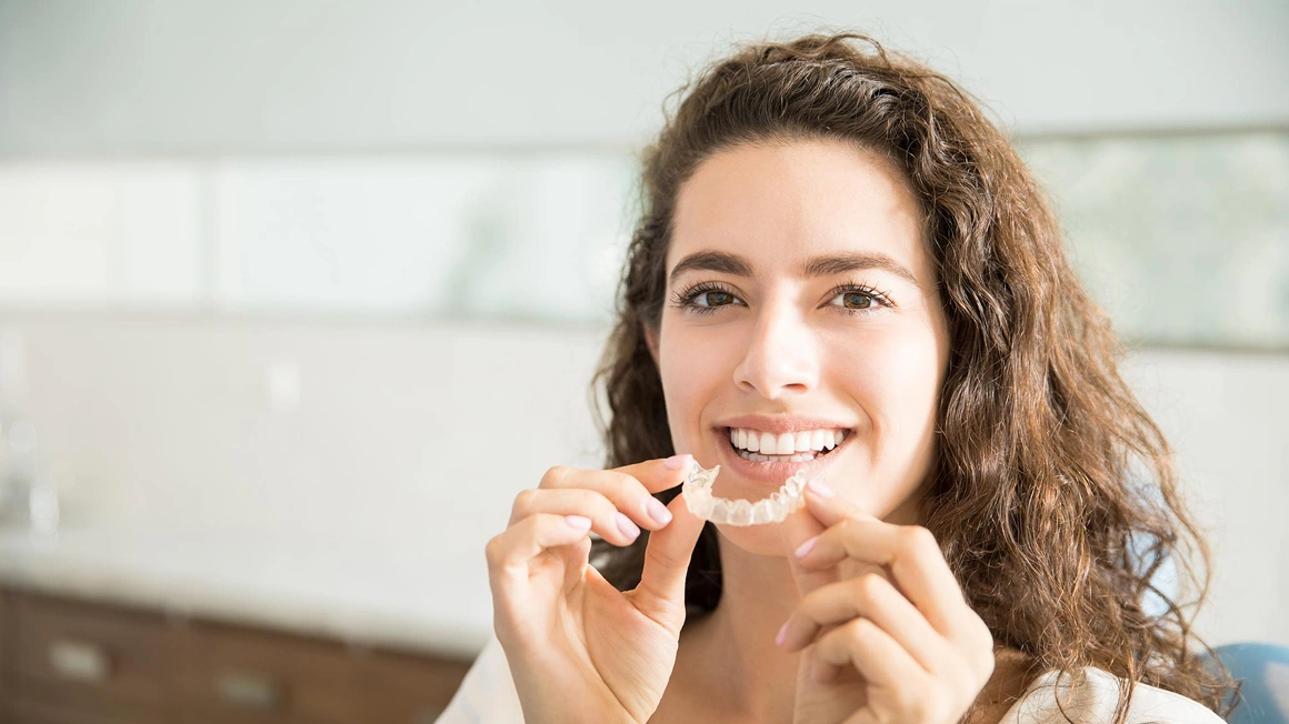 Woman holding clear aligners comparing Invisalign vs Braces for teeth straightening
